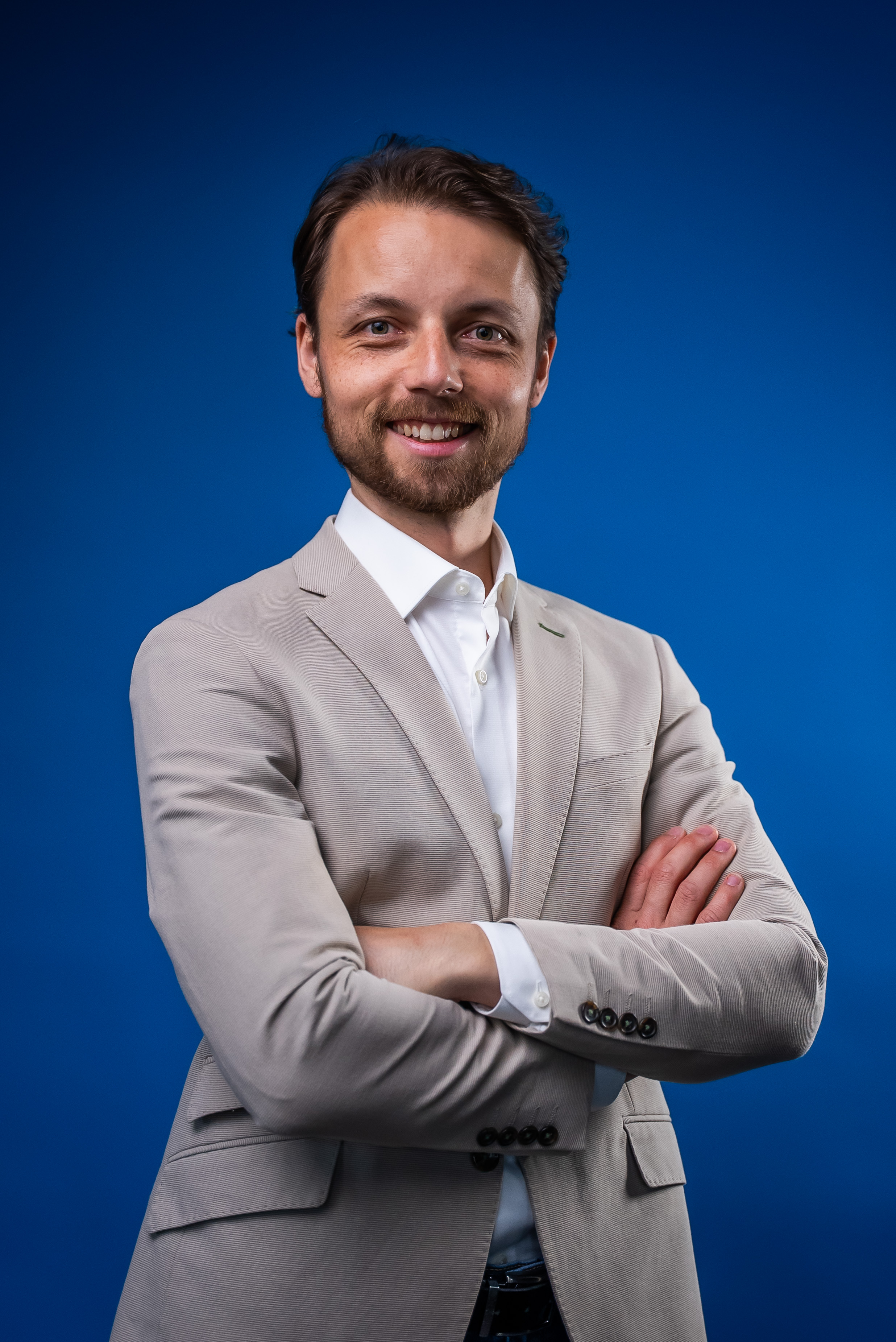 Charles, the person behind Carda, smiling in a light suit against a blue background.
